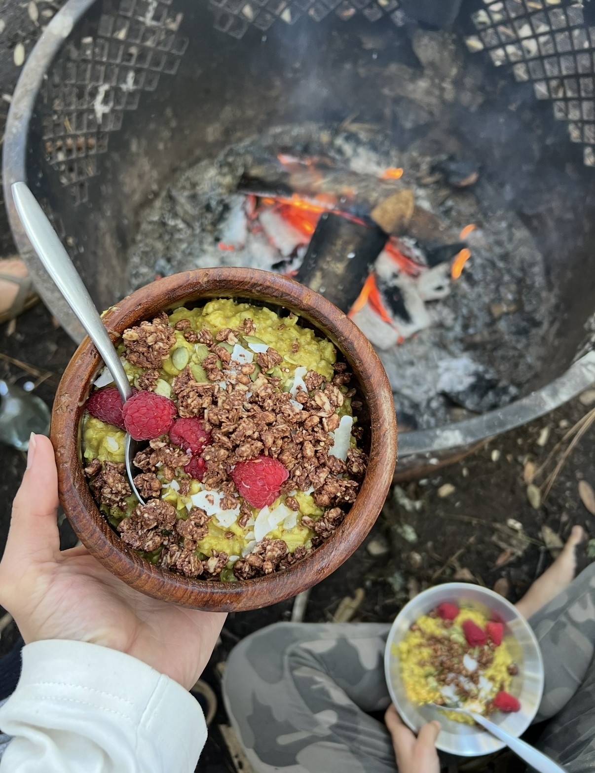 Healthy breakfast bowl with granola and fruit held by campfire