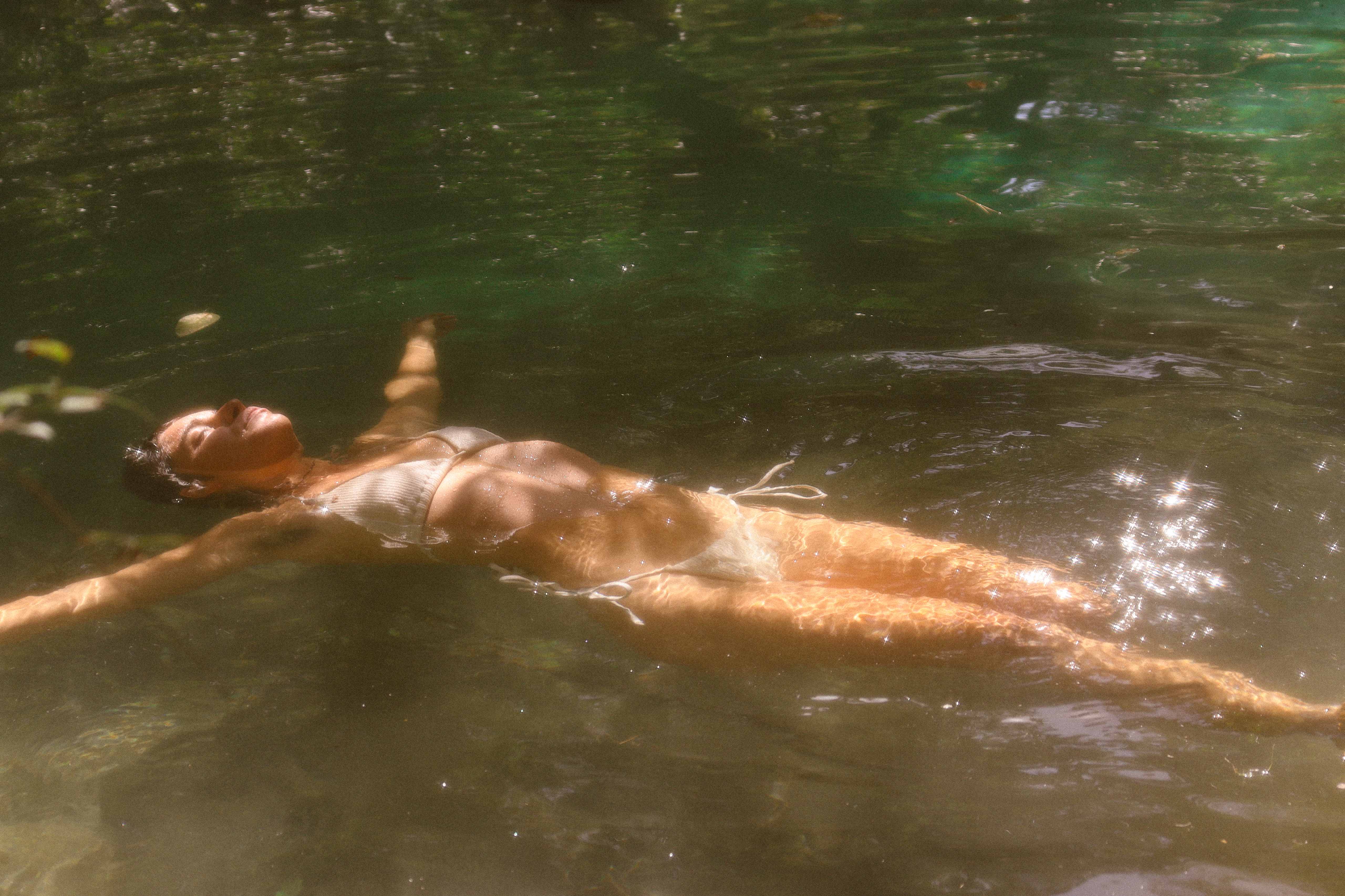 Woman floating peacefully in crystal clear sacred spring water with golden sunlight